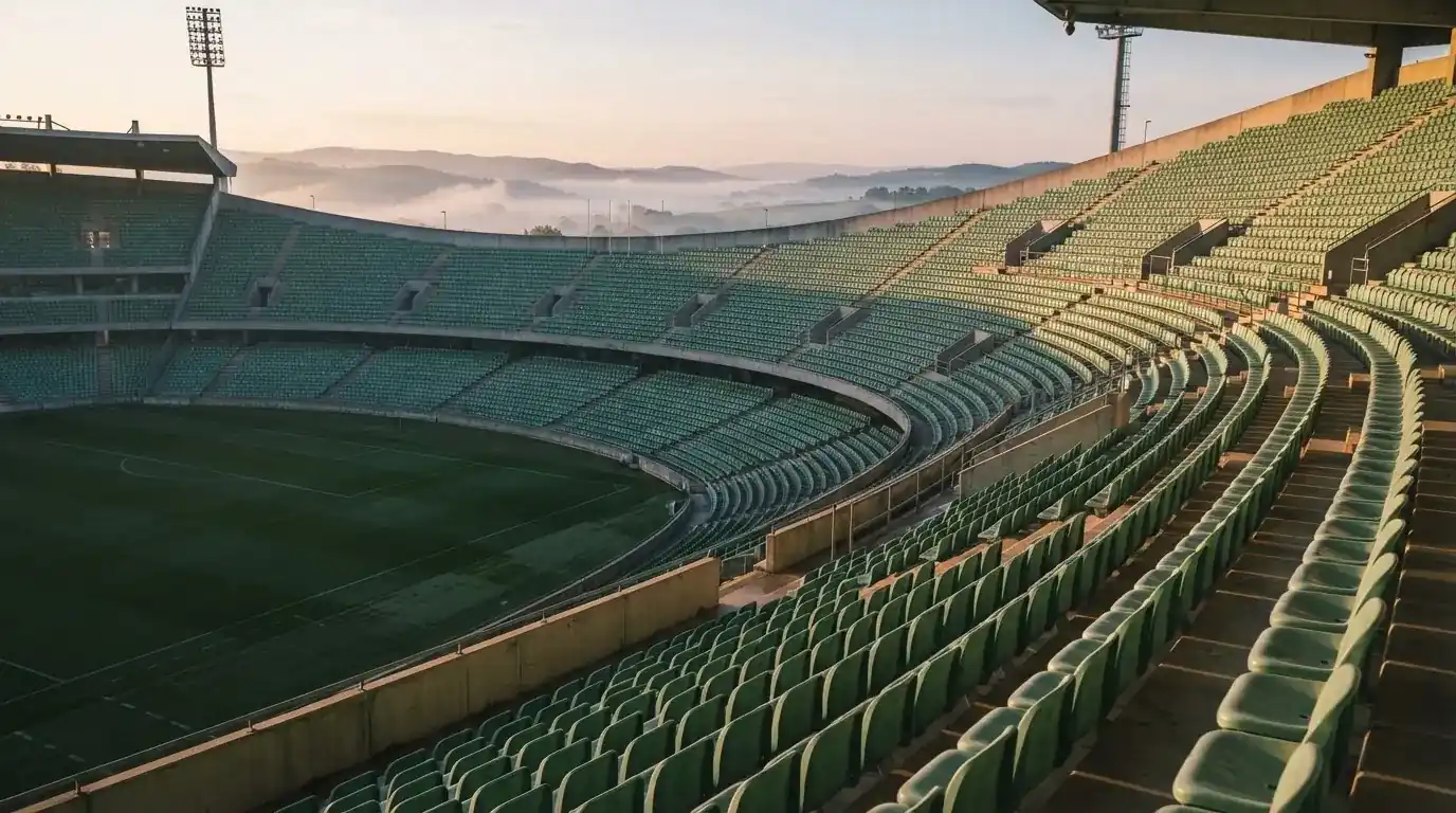 Ein leeres Stadion im Morgenlicht mit Blick auf die Sitzreihen, im Hintergrund Hügel und aufsteigender Nebel.